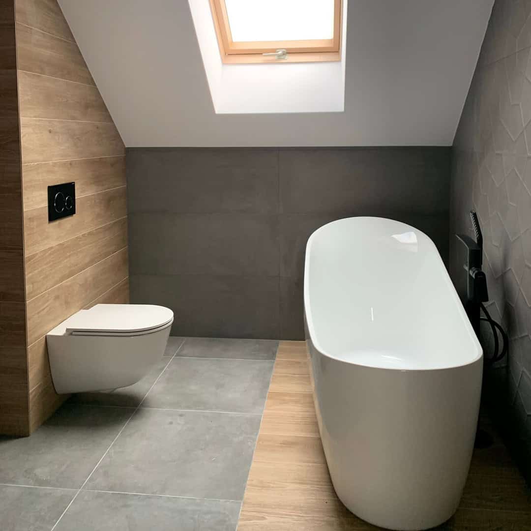 Freistehende weiße Badewanne und Wand-WC unter einem Dachfenster bei einem Innenausbau im Kreis Oberhavel.